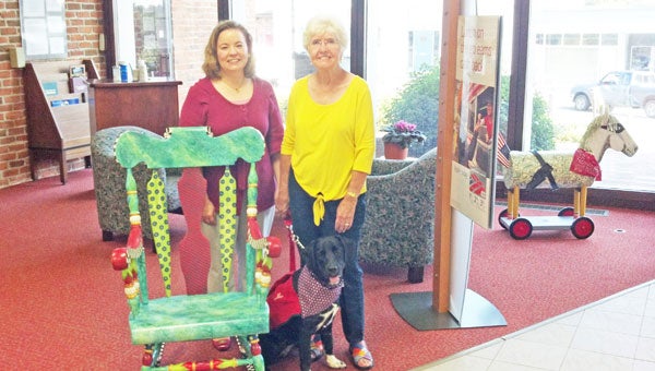 Taken at Bank of America in Tryon is the chair for the silent auction, with Heidi Trim, left, and chair artist Peggie Armstrong, right, and Star, formerly Socks. (photo submitted by Sev Bennett)