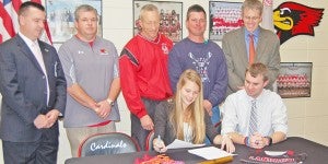 Paige Herbst signs as her father Greg Herbst, back middle, and coaches look on.