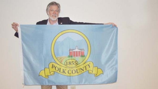 Polk County is considering a new flag to represent the county. County commissioners sponsored a contest, with the winner being Chris Morris. A committee made some changes with the proposed flag presented to commissioners on Monday, April 20. Pictured is Polk's economic development director, who also served on the committee representing the House of Flags, Robert Williamson, displaying the proposed flag. The county is seeking input on the new flag, currently on display in the Womack Building in Columbus. The flag artwork can also be viewed on Facebook at PolkCountyLocalGovernment. (Photo by Leah Justice)